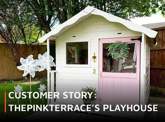 Pink and white playhouse with white windmills and plants