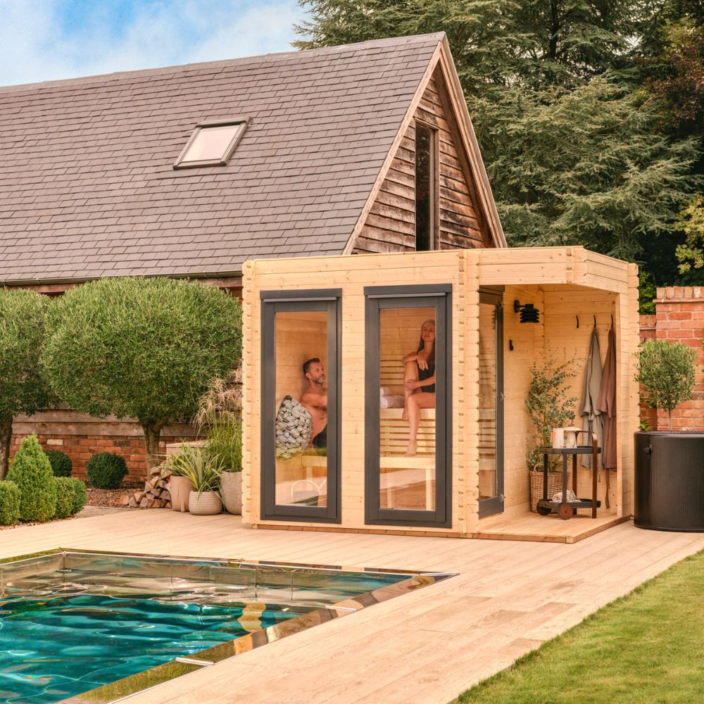 Wooden sauna with glass doors in a backyard setting with a pool and garden.