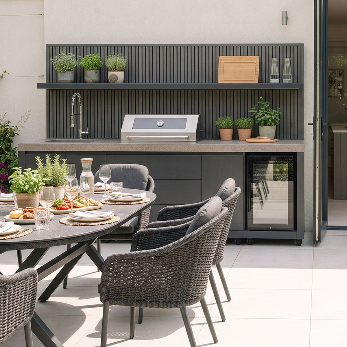 Waltons Strata Signature Outdoor Kitchen in Grey behind an outdoor dining table on a sunny terrace