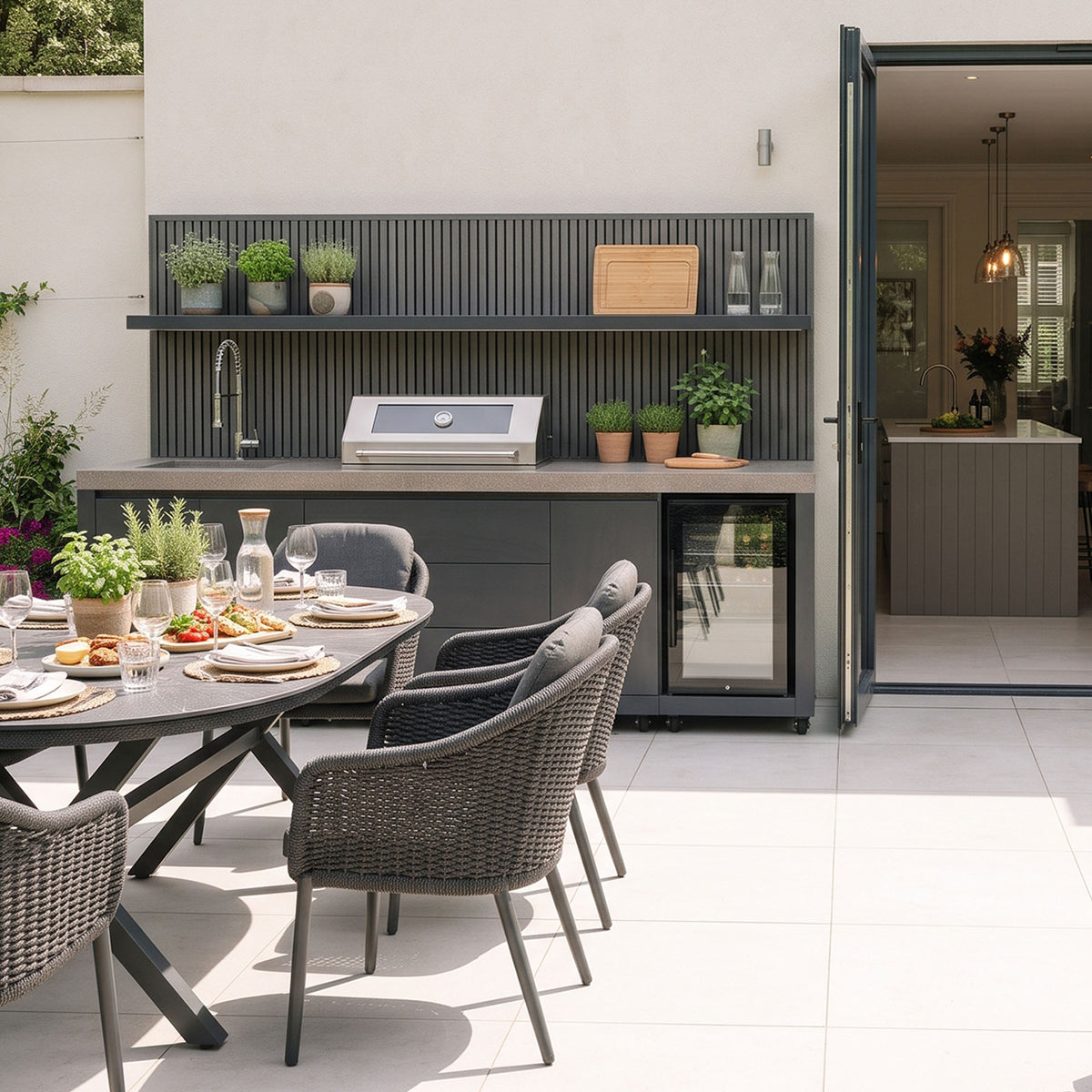 Waltons Strata Signature Outdoor Kitchen in Grey on a pale stone patio next to open bifold doors