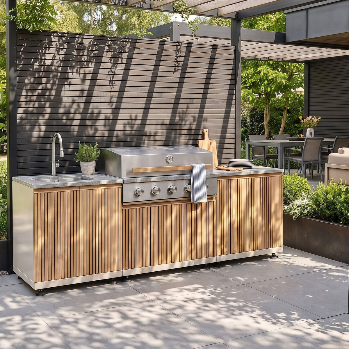 Skogen Small Outdoor Kitchen with Sink in Latte, with slatted door fronts and a grey worktop, under a pergola on a sunny patio#colour_latte