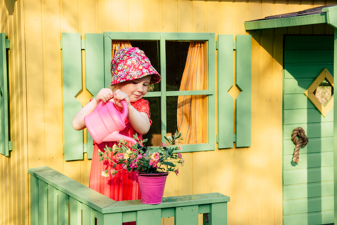 Little girl watering plants outside playhouse