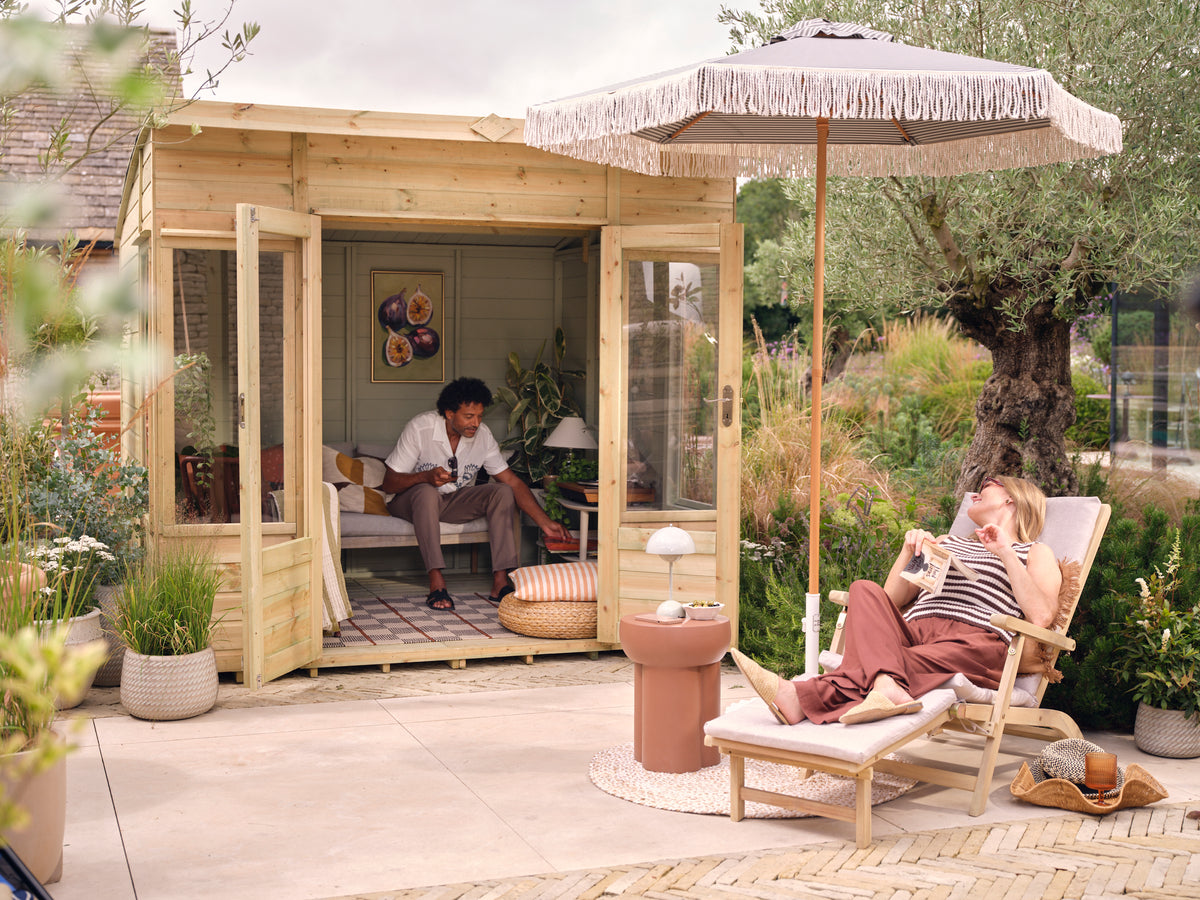 Two people in a garden setting with a wooden summer house and outdoor furniture.