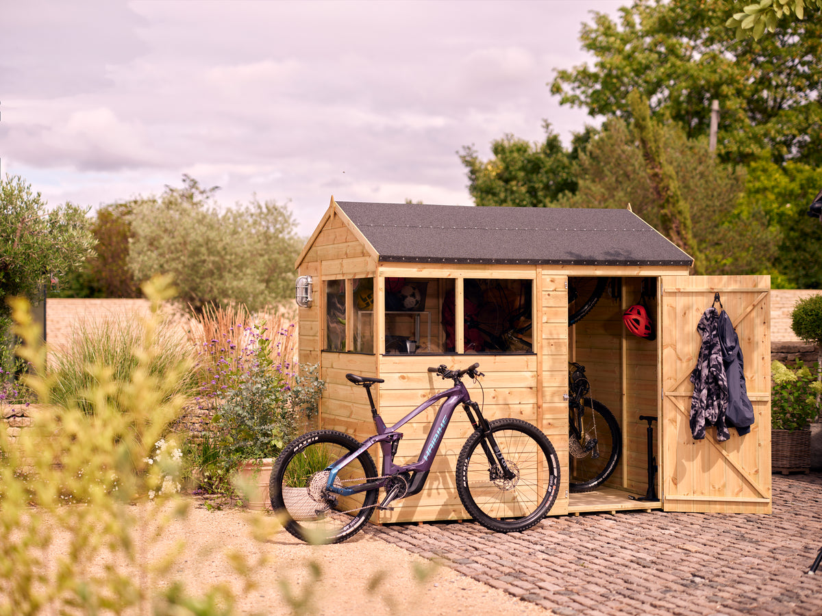 Wooden shed with a bicycle inside, surrounded by greenery