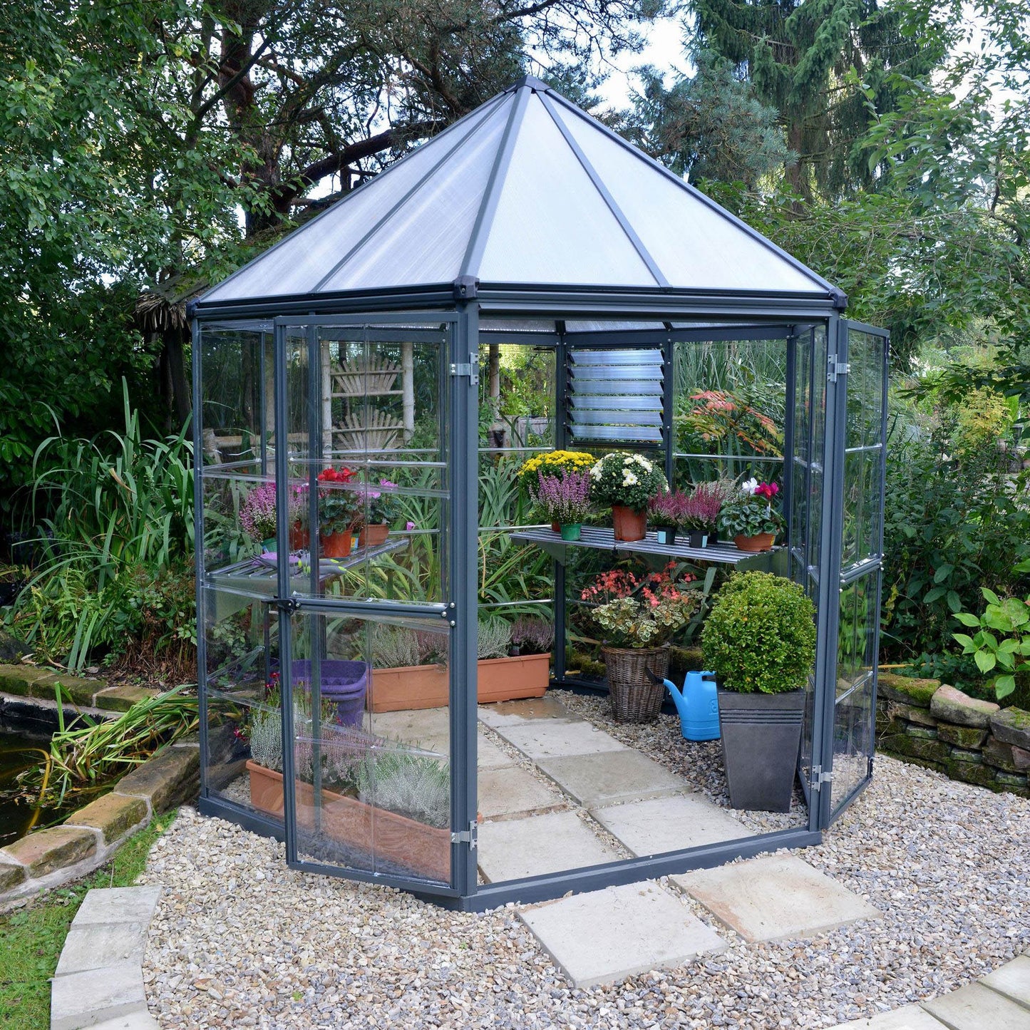 A hexagonal greenhouse with built in shelves and grey metal framing