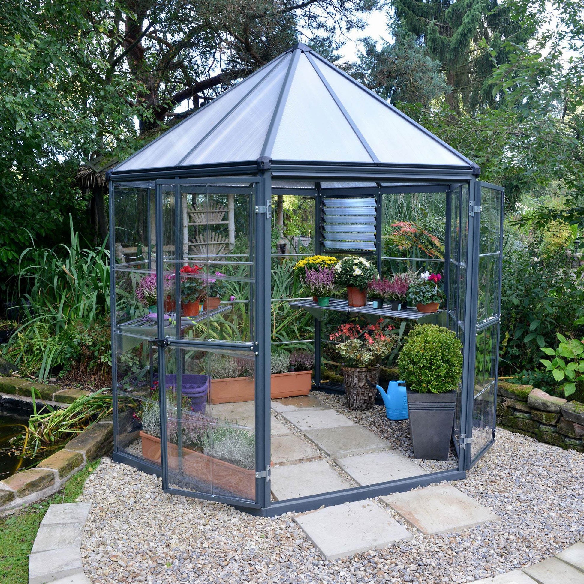 A hexagonal greenhouse with built in shelves and grey metal framing