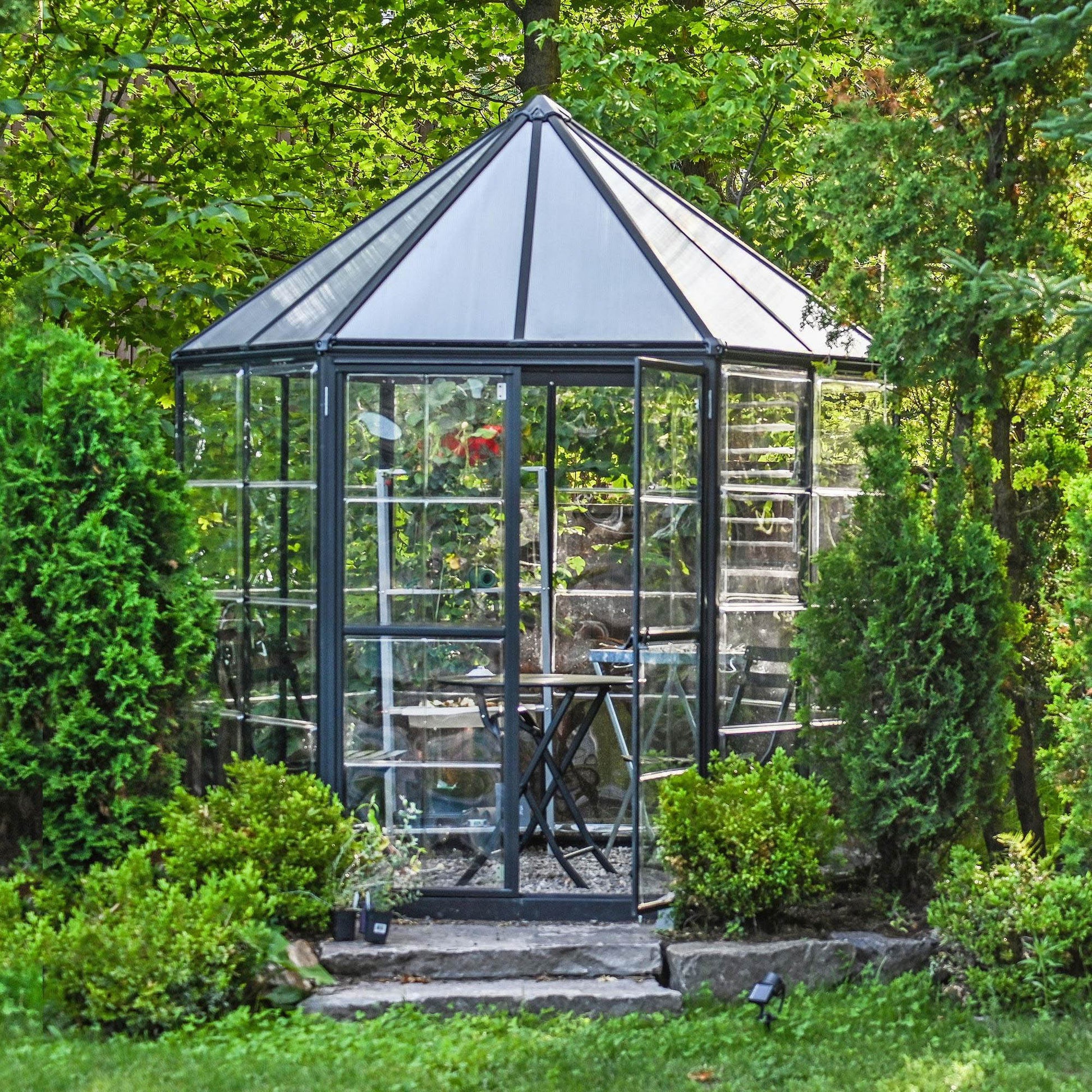 A hexagonal greenhouse with built in shelves and grey metal framing