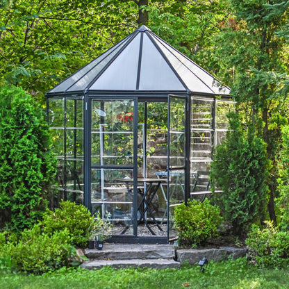 A hexagonal greenhouse with built in shelves and grey metal framing