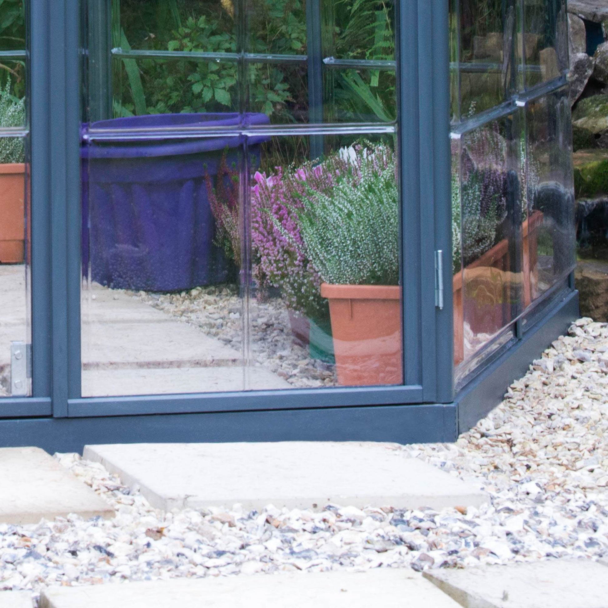A hexagonal greenhouse with built in shelves and grey metal framing